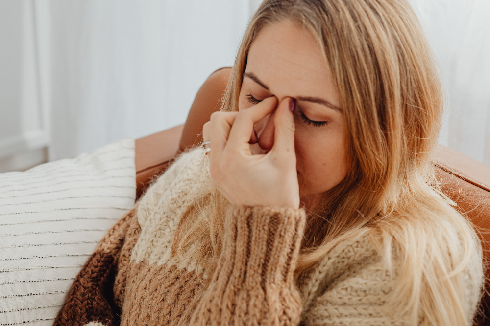 Nainen istuu sohvalla silmät suljettuina ja puristaa sormillaan nenänvarttaan – ilme kertoo jännityksestä